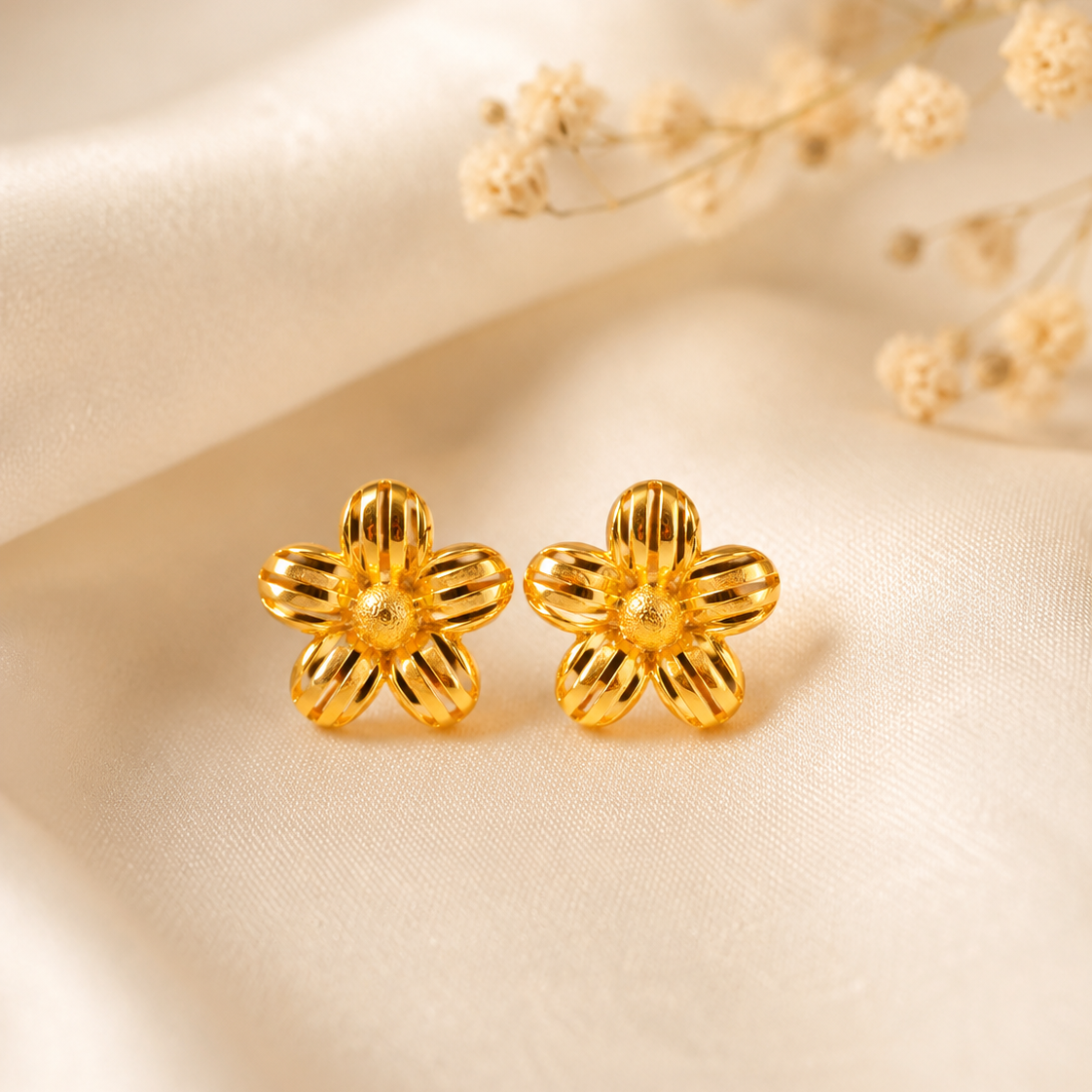 Gold flower-shaped earrings on a beige fabric background with dried flowers.