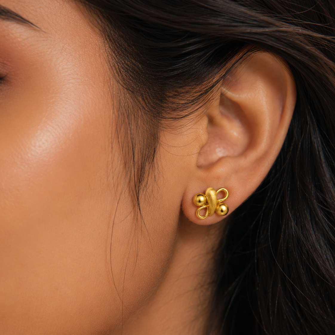 Close-up of a woman's ear wearing a gold earring with a blurred background