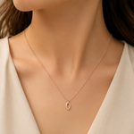 Rose gold necklace with a delicate pendant on a person wearing a white top.