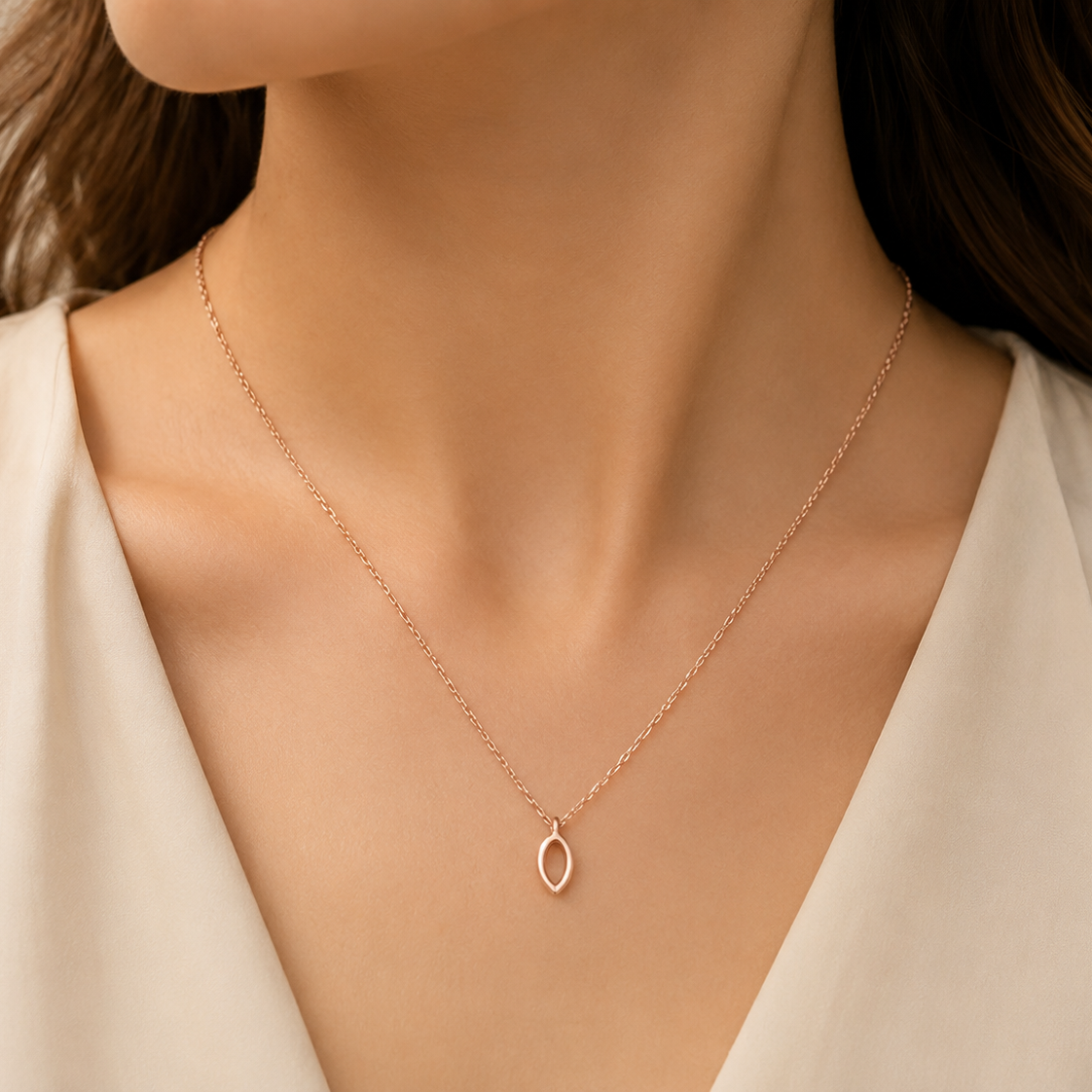 Rose gold necklace with a delicate pendant on a person wearing a white top.