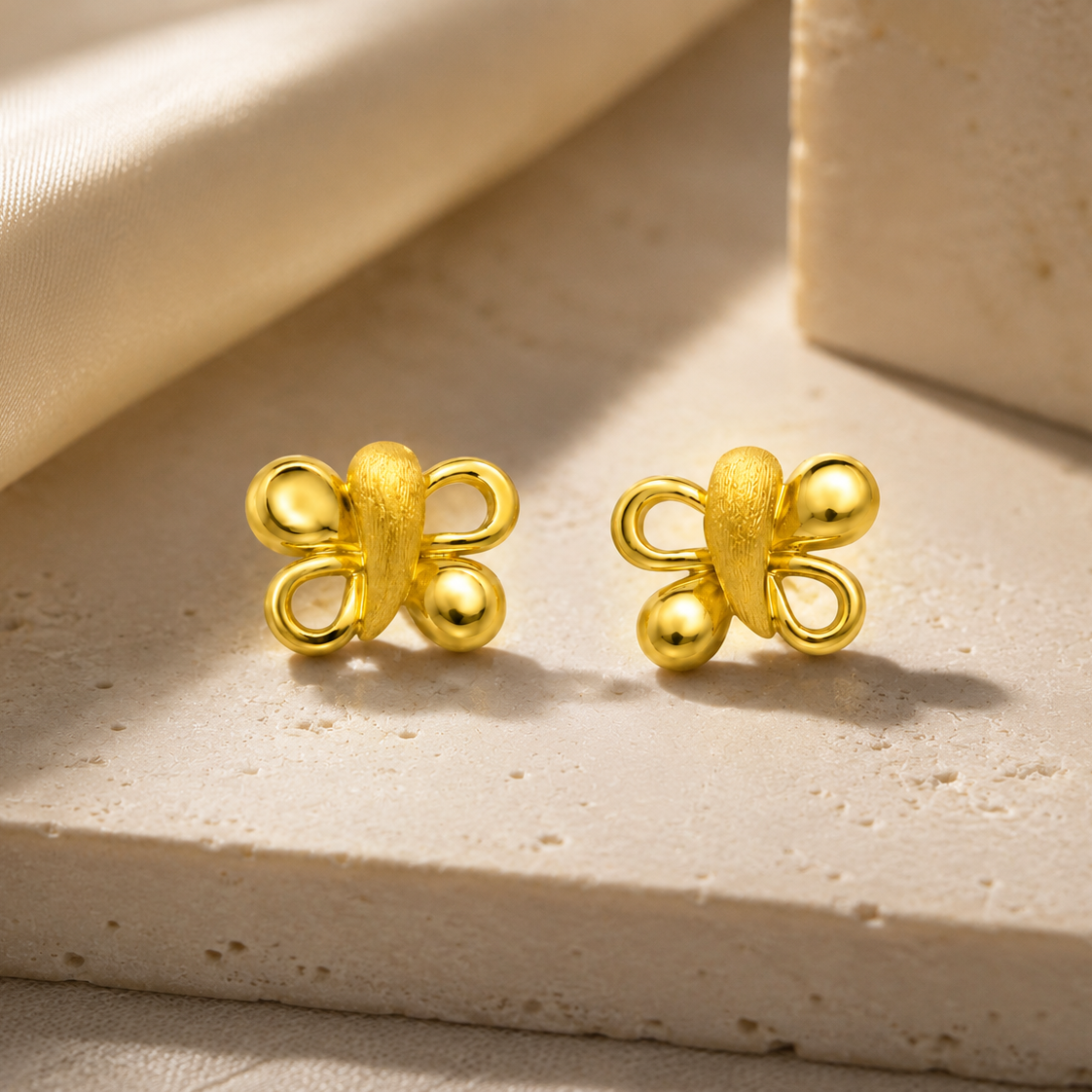 Pair of gold butterfly-shaped earrings on a beige fabric background